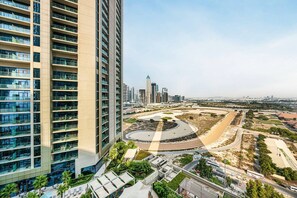 A high-rise building with multiple floors, a landscaped area with pathways and greenery, and a distant city skyline. - Stylish 2BR with Canal Views in Business Bay (Dubai)