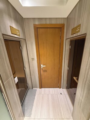 A hotel bathroom with a wooden door, a shower area, and a toilet. - Stylish 2BR with Canal Views in Business Bay (Dubai)