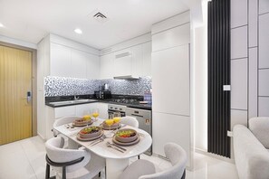 A modern kitchen with white cabinetry, a black and white backsplash, and a dining area with a table set for four. - Skyline View Apt in Business Bay w/Pool & Sauna (Dubai)
