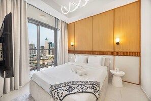 A hotel room with a large bed, a television, a view of the cityscape, and a modern light fixture. - Skyline View Apt in Business Bay w/Pool & Sauna (Dubai)