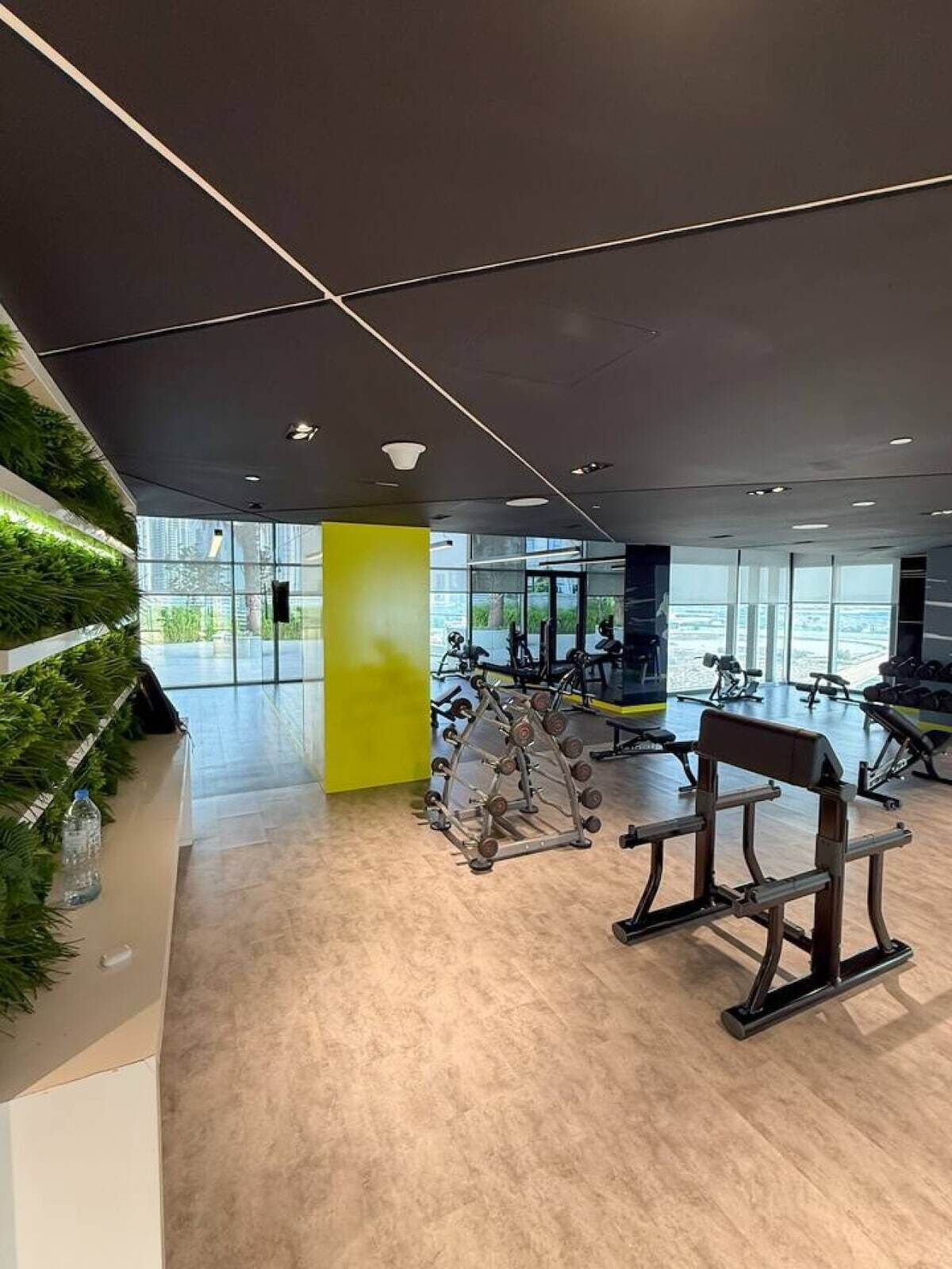 Ett modernt gym med träningsutrustning, en grön vägg och stora fönster.