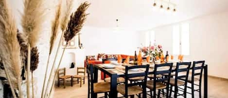 Un comedor con una mesa y sillas de madera, una araña y una ventana que deja entrar luz natural.