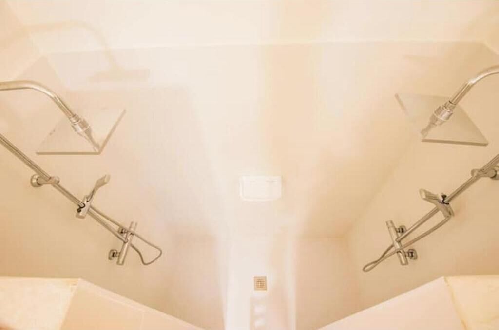 Une salle de bain équipée de deux pommes de douche et d’un panneau de commande visible.
