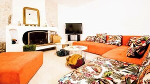 A living room with a fireplace, a television, and a sofa with floral cushions. - "Côté sauvage" 4-star vacation rental for 16 people (La Tremblade)