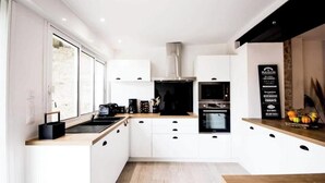 A modern kitchen with white cabinets, a black range hood, and a wooden countertop. - "Côté sauvage" 4-star vacation rental for 16 people (La Tremblade)