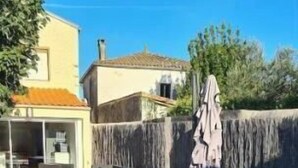 Un patio esterno con tavolo e sedie rossi, una zona salotto coperta e un muro in pietra.