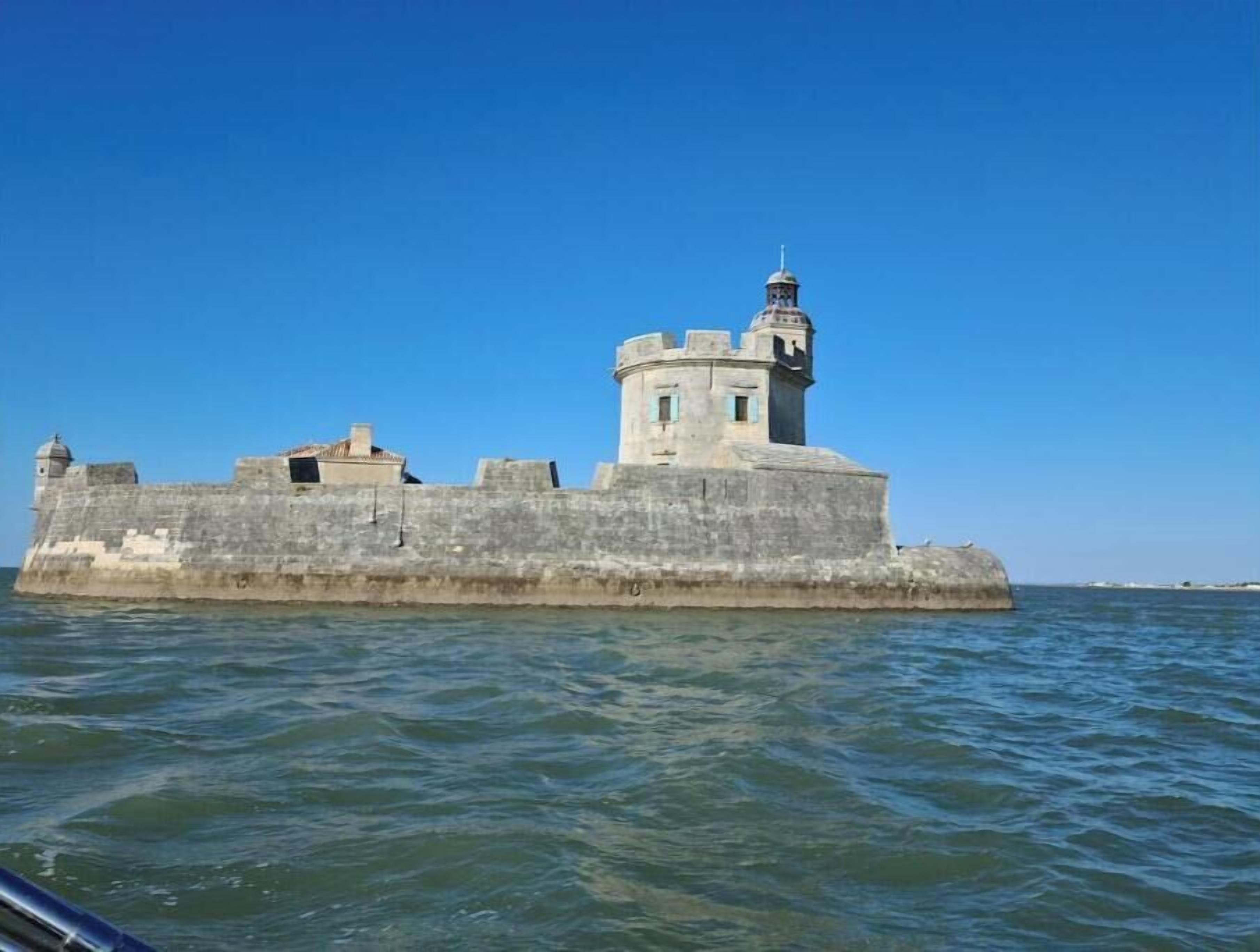 Eine befestigte Anlage mit einem zentralen Turm und einem kleineren Gebäude, umgeben von Wasser.