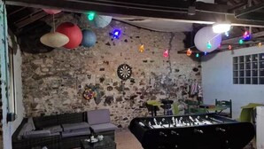 Una stanza con un tavolo da calcio, un divano e un bersaglio da freccette su un muro in pietra.