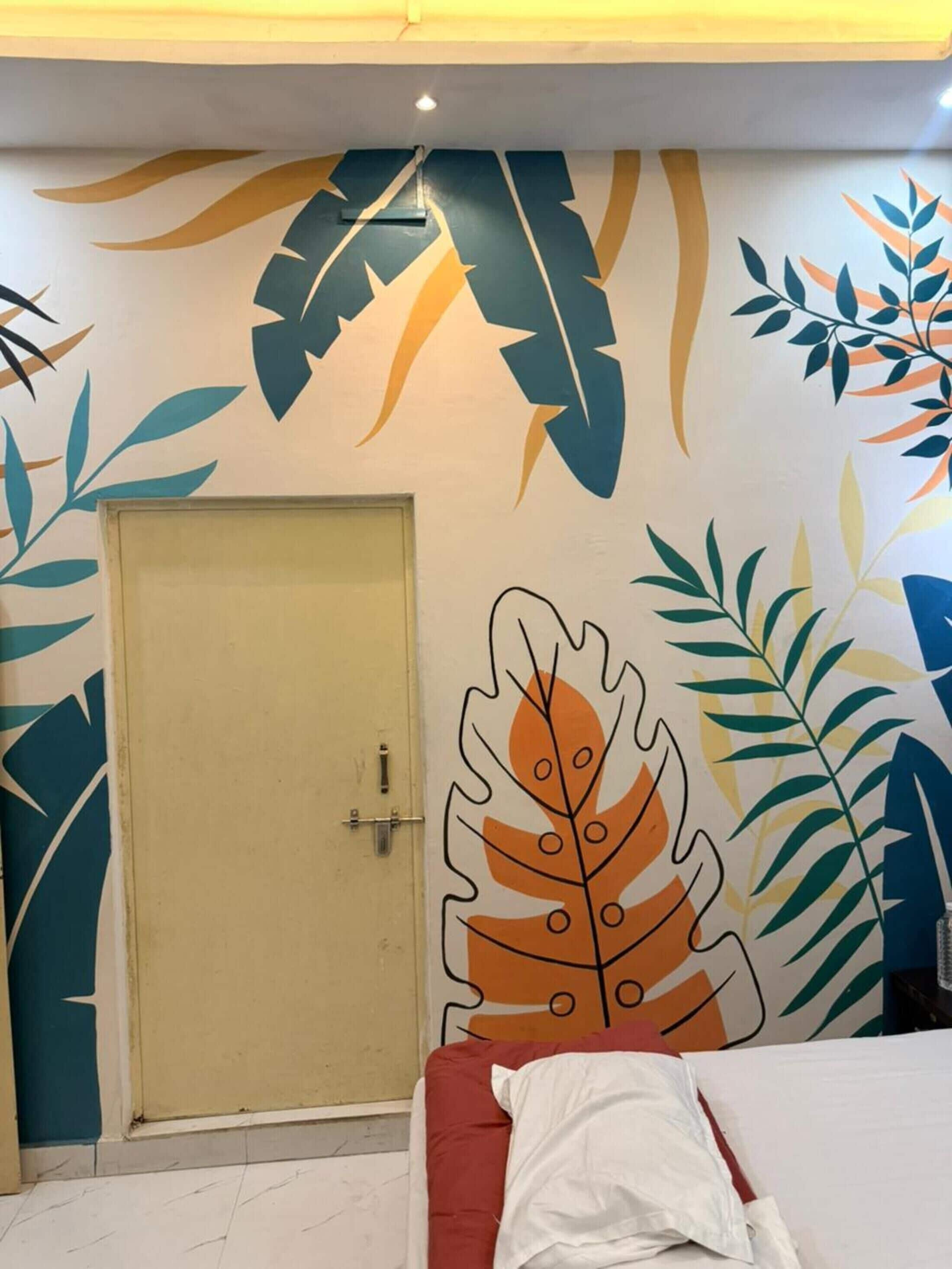 Una habitación con una puerta, una cama con cabecera roja y paredes decoradas con motivos de hojas.