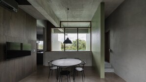Un interior moderno con una mesa redonda y sillas, un televisor de pantalla plana montado en la pared, y un amplio ventanal que ofrece vistas a la vegetación.