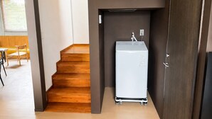 Habitación pequeña con una escalera de madera que sube a un segundo piso, un electrodoméstico blanco y una puerta.