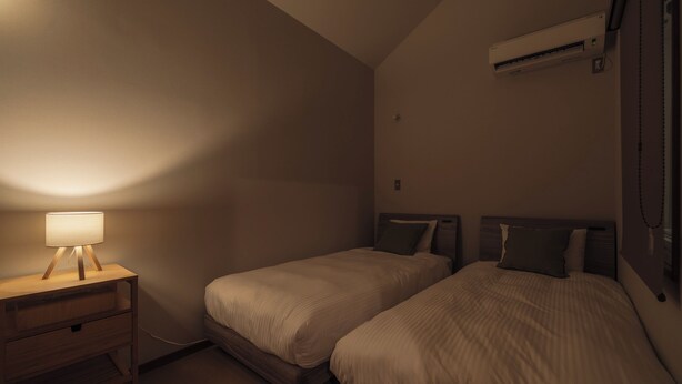 Habitación de hotel con dos camas, una mesita de noche, un equipo de aire acondicionado y una lámpara fijada a la pared.