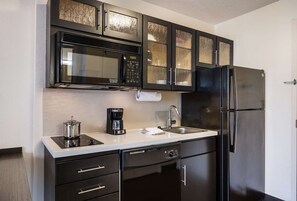 Eine kleine Küche mit Mikrowelle, Kaffeemaschine, Spüle und Kühlschrank.