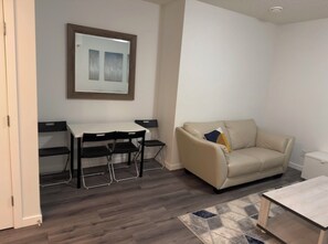 A room with a sofa, a small table, a desk with chairs, and a framed picture on the wall. - Cosy 1 Bedroom Suite in Top Location Near Lake (Calgary)