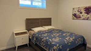 Ein Schlafzimmer mit einem Bett, einem Nachttisch, einem Fenster und einem floralen Gemälde an der Wand.
