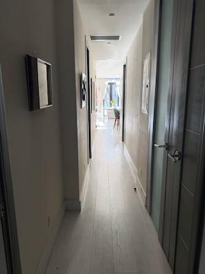 Ein Korridor mit hellem Holzboden, einer Tür rechts und einem Fenster am Ende.