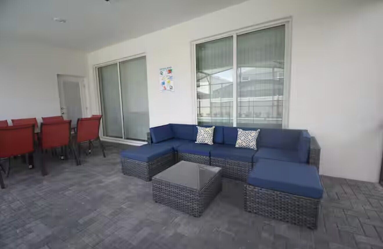 A room with a blue sofa, red chairs, a glass door, and a poster on the wall.