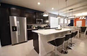 Una cucina moderna con un frigorifero in acciaio inossidabile, un forno a microonde e una grande isola con sgabelli da bar.