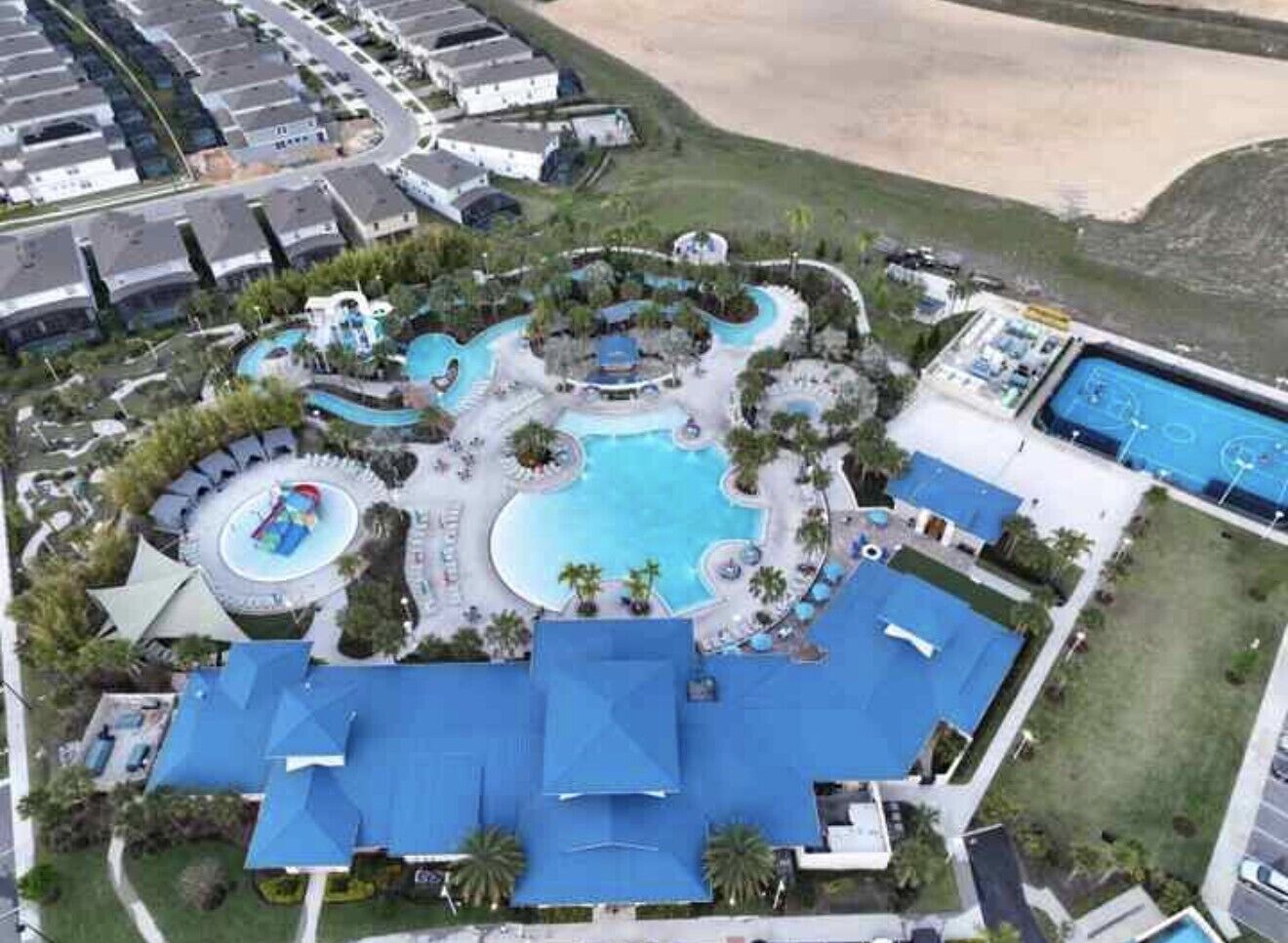 An aerial view of a resort with multiple swimming pools, a central water feature, and a large building with a blue roof.