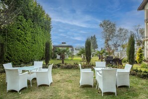 Un espacio de estar al aire libre con mobiliario de mimbre blanco y una estructura de pérgola.