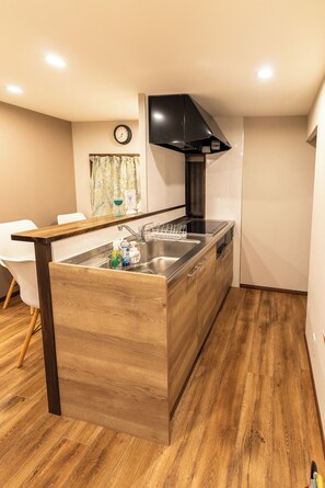 A modern kitchen with a wooden island, stainless steel appliances, and a black range hood. - Direct from Kansai Airport | 8-minute walk from Tenka-chaya | Quiet, private 40 m² rental | Accommodates up to 2 people | Easy access to Namba, Shinsaibashi, and Umeda | Includes a bathtub and kitchen (Nishinari-ku)