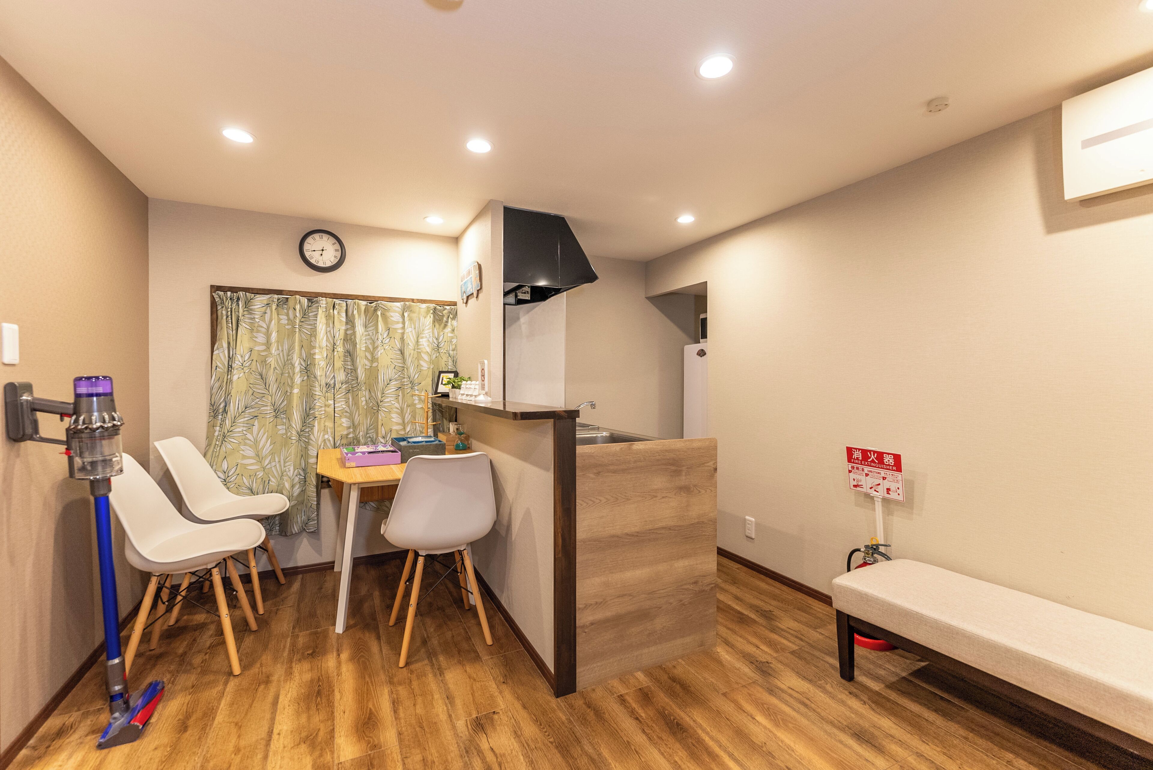 A compact kitchenette with a sink, a clock, and a fire extinguisher sign.