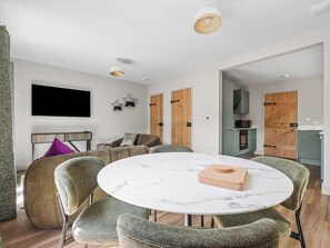 Ein modernes Wohnzimmer mit einem runden Marmortisch, grünen Polstersesseln, einer Couch und einem an der Wand montierten Fernseher.