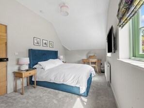 Ein Schlafzimmer mit einem Bett, einem Schreibtisch, einem Stuhl, einem Fernseher und einem Fenster mit Vorhängen.