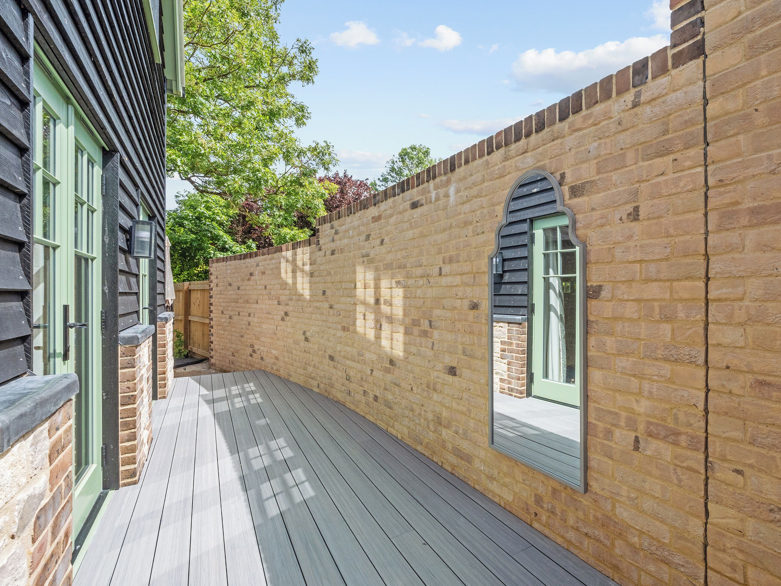 A narrow outdoor corridor with a wooden deck, brick walls, and a door with a green frame.