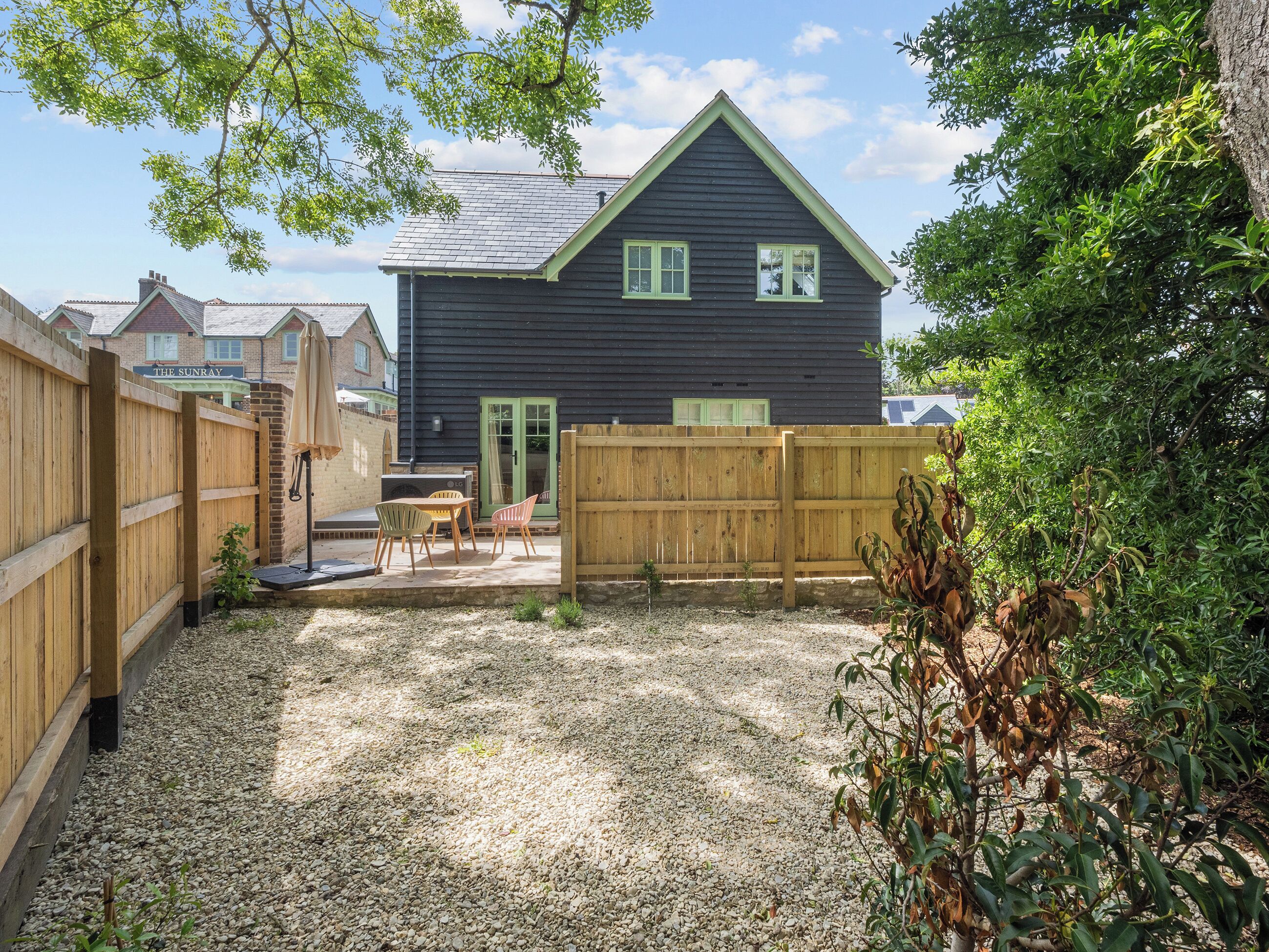 A backyard with a wooden fence, a barbecue area, and a house with a dark exterior and green trim.
