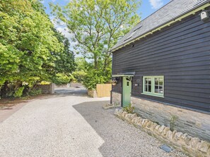 Un bâtiment avec une allée de gravier menant à une porte en bois, entouré d’arbres et d’un mur de pierre.