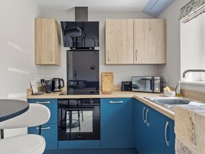 A compact kitchen with a microwave, toaster, kettle, and a small dining area with a table and chairs. - The Milk Palour - UKC9938 (Weymouth)