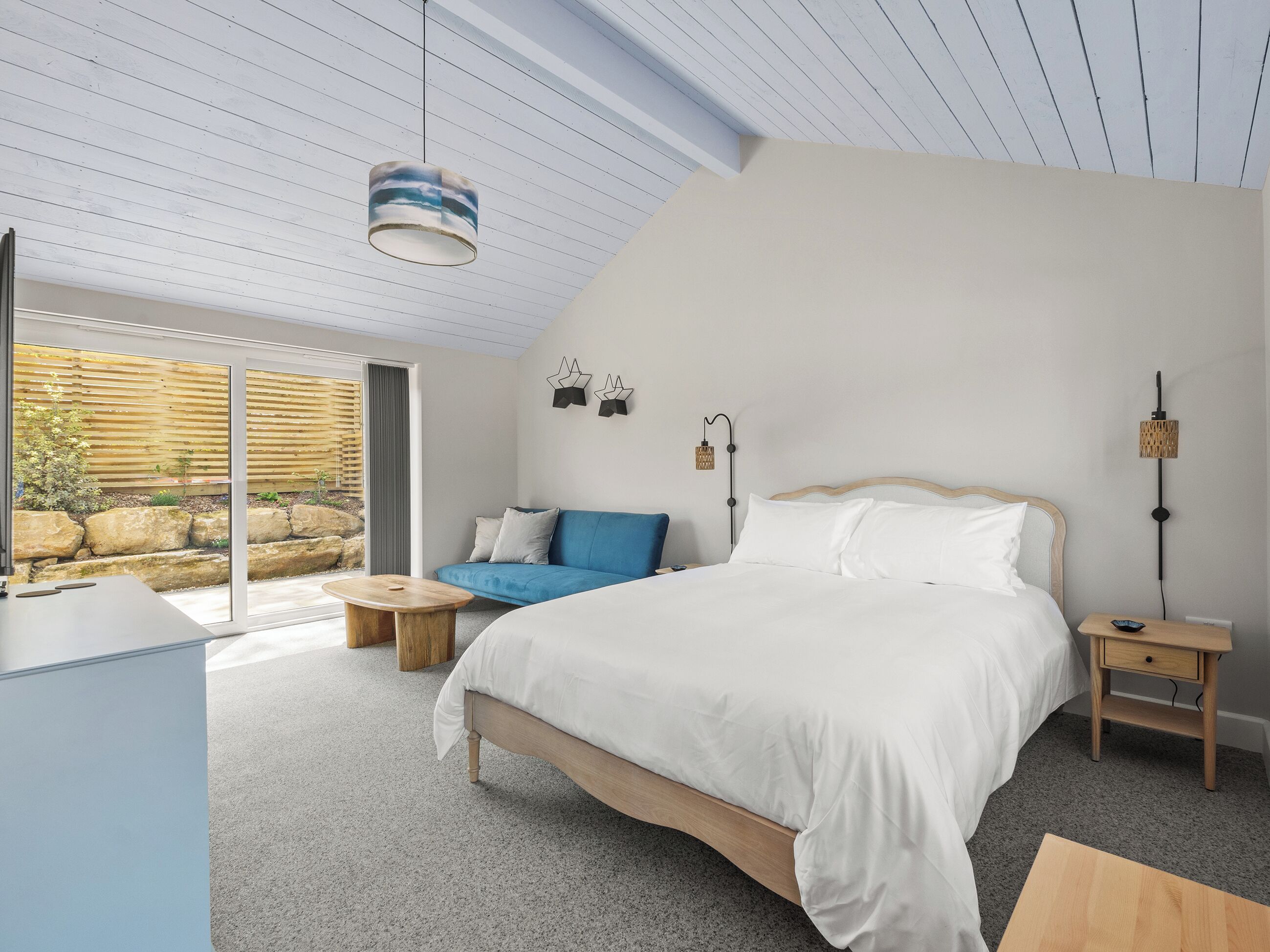 A bedroom with a bed, bedside tables, a nightstand, a window, and a view of the outdoors.