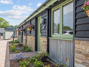A building with a stone foundation, green window frames, and hanging flower baskets. - The Milk Palour - UKC9938 (Weymouth)