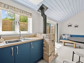 A modern kitchen with a sink, cabinets, and a stone feature. There is a dining area with a table and chairs. - The Milk Palour - UKC9938 (Weymouth)