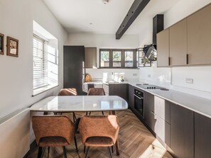 A modern kitchen with a dining area, featuring a marble countertop, wooden flooring, and built-in cabinets. - Solstice Stables - UKC9940 (Dorset, Weymouth, Osmington)