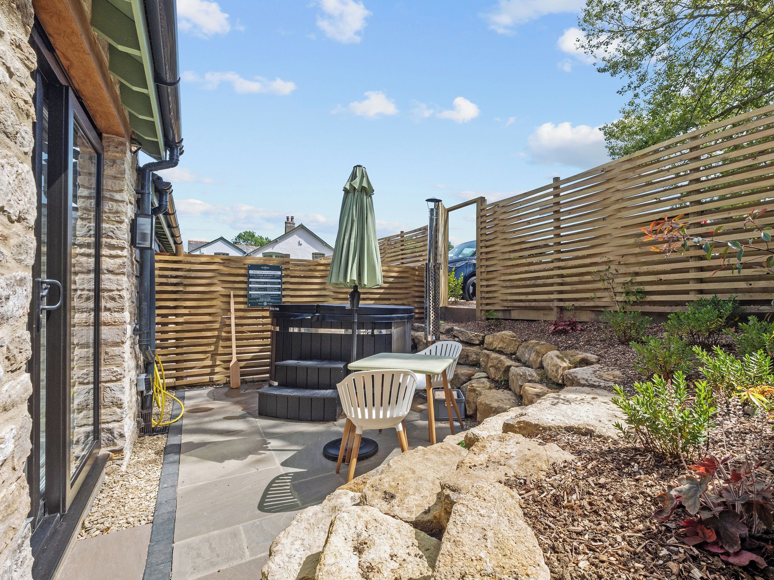 A patio area with a stone wall, a wooden fence, a table with chairs, and a green umbrella.