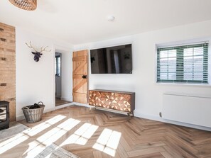 A modern living room with a herringbone floor, a wooden cabinet, a mounted TV, and a fireplace. - Suncrest Cottage - UKC9942 (Weymouth)