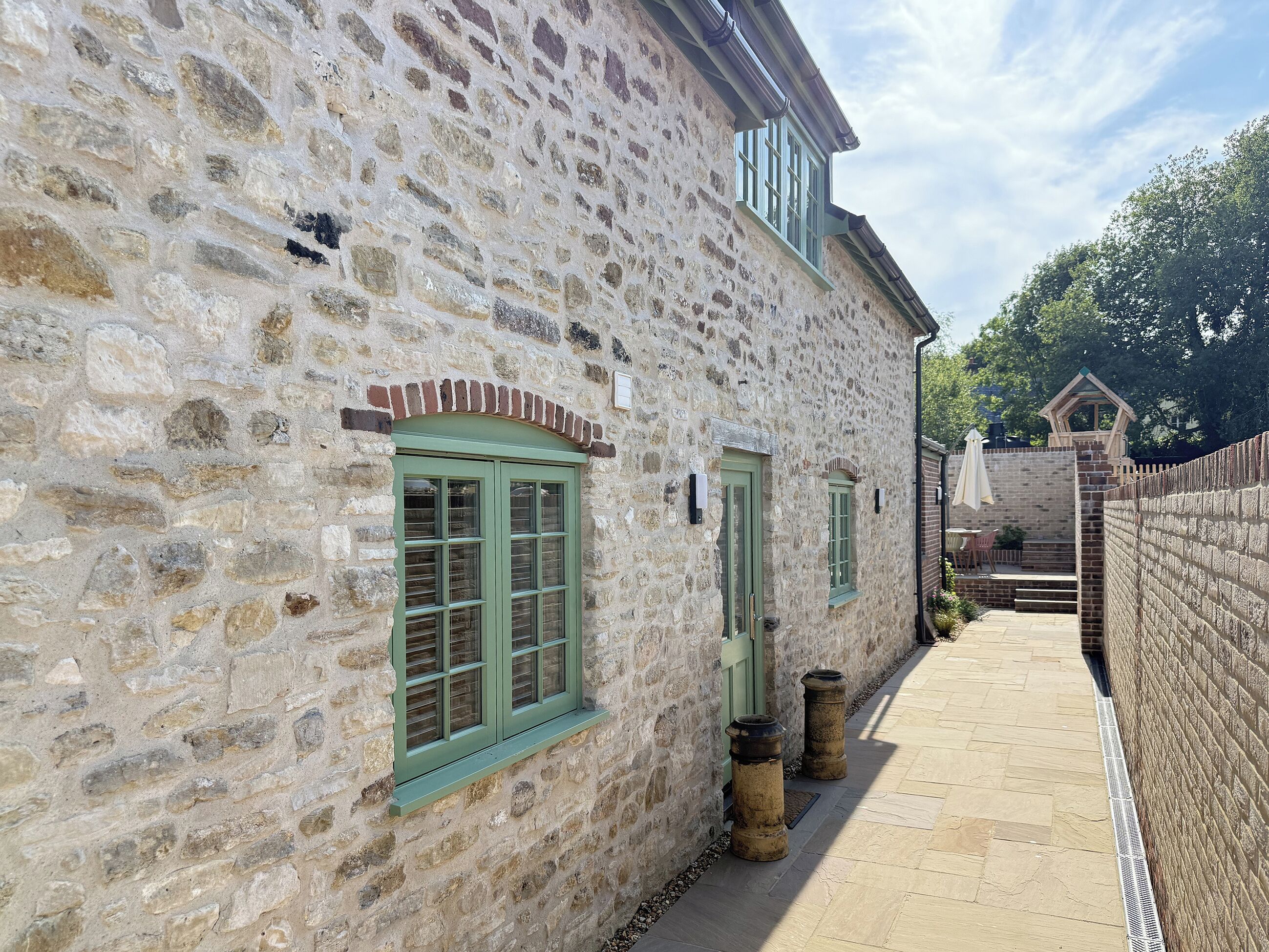 A stone building with a narrow pathway, a small window with shutters, and a brick wall.