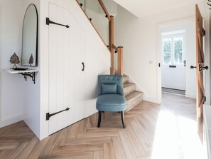 A room with a herringbone wood floor, a blue armchair, a white wardrobe with black handles, and a wooden staircase. - Suncrest Cottage - UKC9942 (Weymouth)