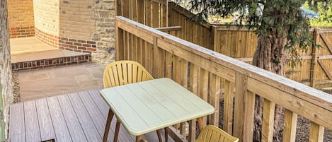 Una terraza de madera con una mesa y dos sillas, rodeada por una valla de madera y un muro de ladrillo.