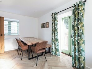 A dining area with a wooden table and chairs, a window with blinds, and a door with a green frame. - Suncrest Cottage - UKC9942 (Weymouth)