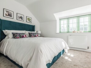 A bedroom with a bed, a headboard, a window with blinds, and a radiator. - Suncrest Cottage - UKC9942 (Weymouth)