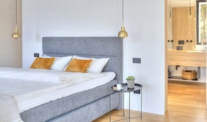 Een moderne slaapkamer met een grijs gestoffeerd bed, een klein nachtkastje met een plant, en een nachttafeltje.
