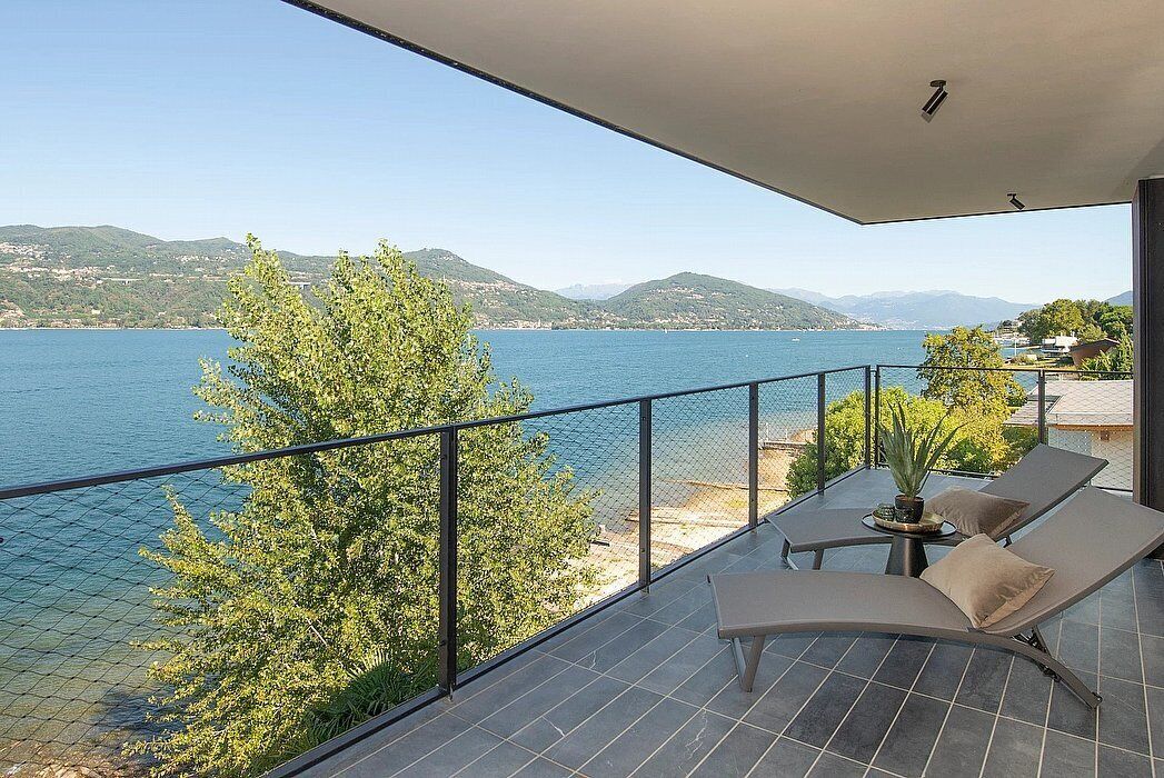 Un balcón con vista a un lago y montañas, amueblado con una mesa y dos sillones.