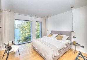 Un dormitorio moderno con una cama grande, una silla, una mesita y vistas al exterior.