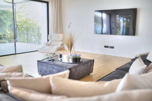 A modern living room with a sofa, a coffee table with decorative items, a white armchair, and a flat-screen TV mounted on the wall. - Villa Ronia: An elegant and modern four-story villa located right on the Lake Maggiore, with Free WI-FI. (Angera)