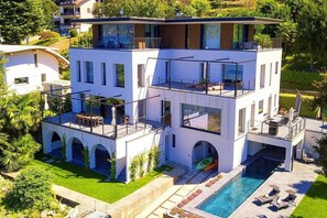 A modern multi-story house with a swimming pool, outdoor seating, and a view of the surrounding landscape. - Villa Ronia: An elegant and modern four-story villa located right on the Lake Maggiore, with Free WI-FI. (Angera)