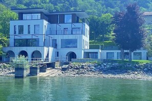 A modern multi-story building with a waterfront view, featuring balconies and a bridge leading to the water. - Villa Ronia: An elegant and modern four-story villa located right on the Lake Maggiore, with Free WI-FI. (Angera)