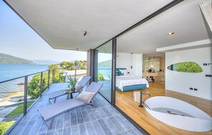 Un dormitorio moderno con un ventanal grande, una bañera y un balcón con vistas al lago.